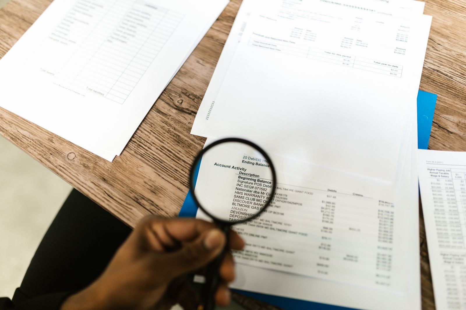 A hand holding a magnifying glass over a printed document on a desk.