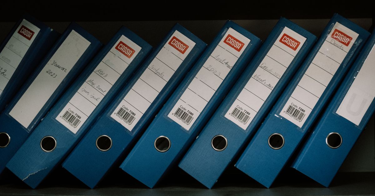 Rows of blue office binders on a shelf, each labeled with dates and names.