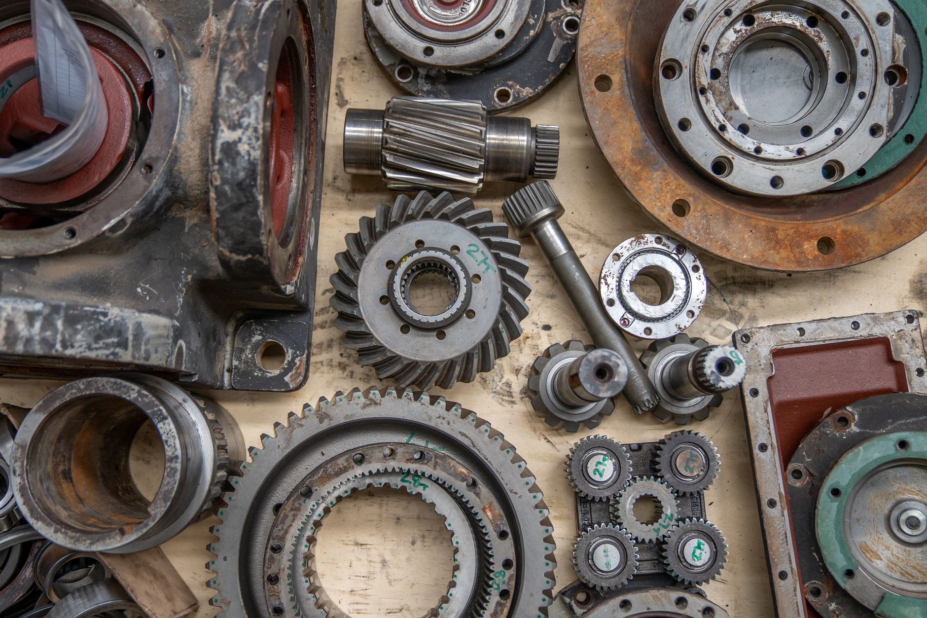 Gears, shafts, bearings, and housings from one gearbox laid out on a workbench, separate parts of a single system.