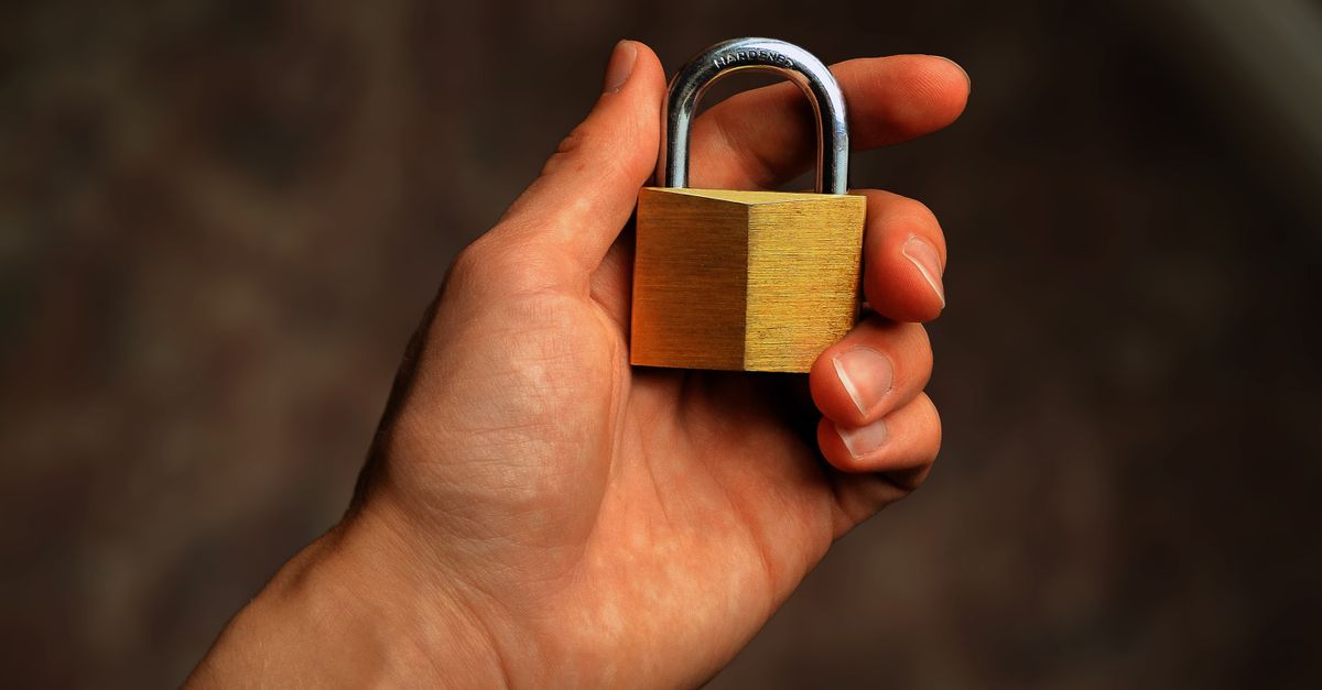 A hand holding a brass padlock, closed and centered against a plain background.