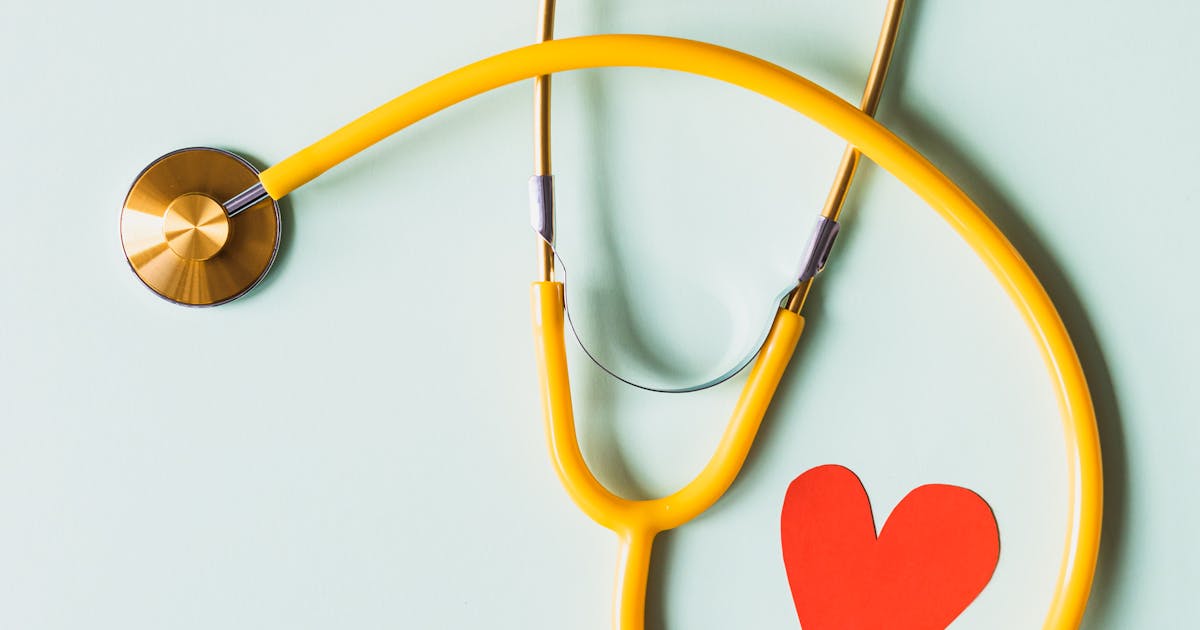 Yellow stethoscope and red paper heart on a mint-green background — representing HIPAA and GDPR health data compliance.