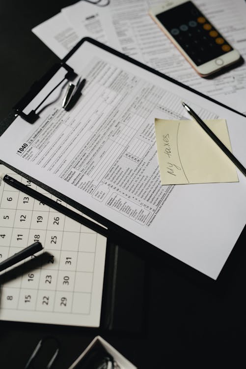 Clipboard with tax forms and a pen on a dark desk — representing the documentation auditors review in a SOC 2 assessment.