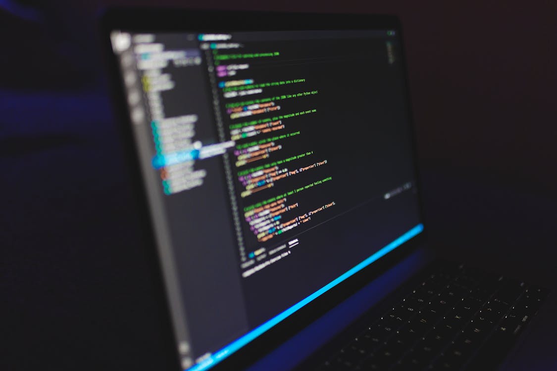 Dark laptop displaying colorful code in a dim room — representing a SOC 2 compliance review.